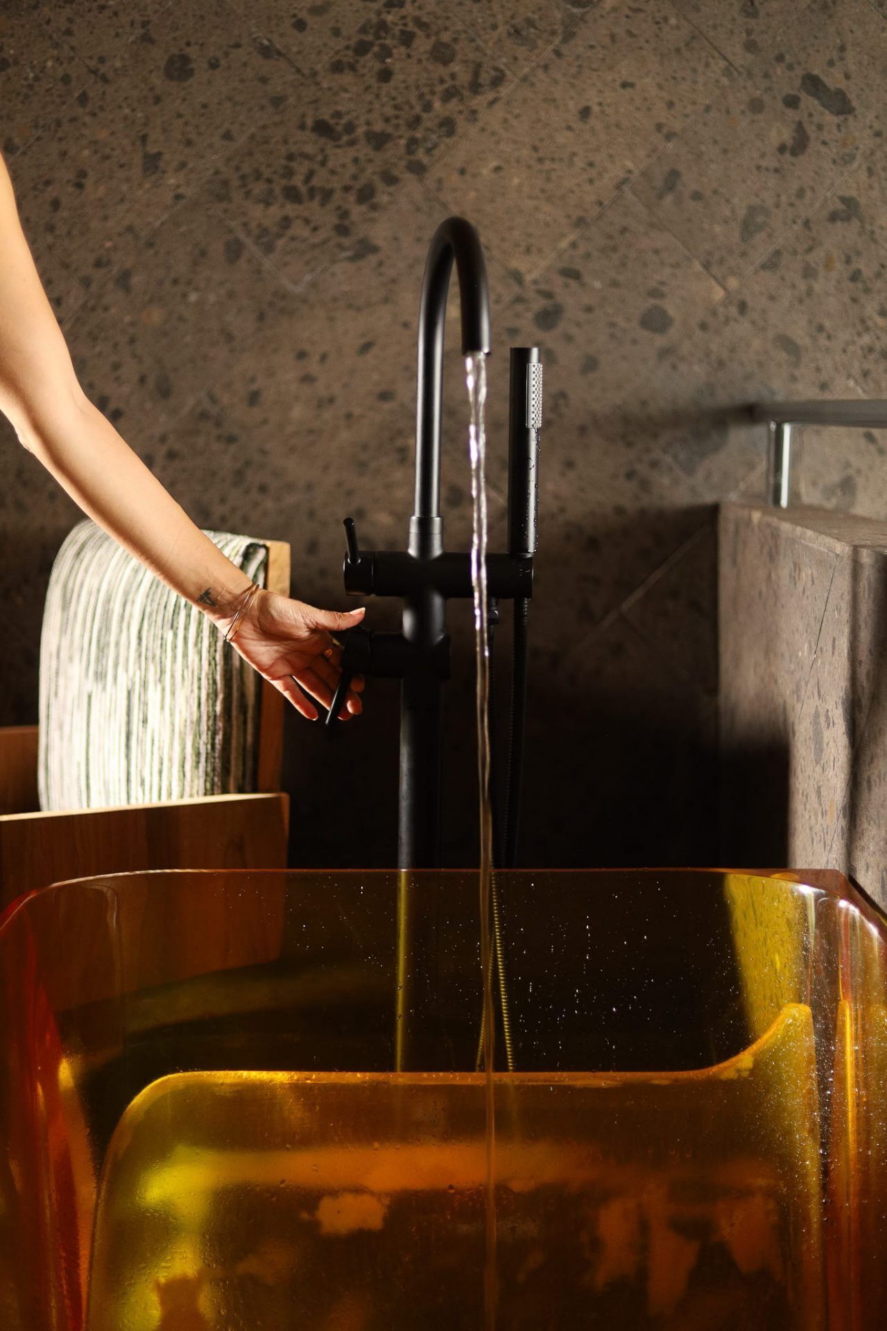A hand turning a faucet with water flowing into a clear container.
