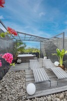 Un jardín en la azotea con terraza de madera, sillas de descanso, un jacuzzi y plantas en macetas.