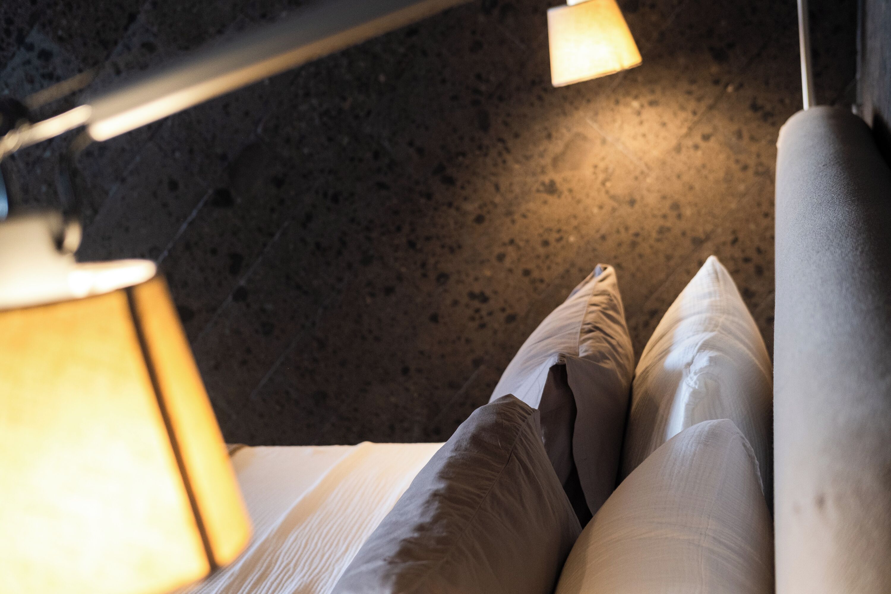 Un gros plan d’un lit avec du linge de lit blanc, un oreiller, une lampe et un sol à motifs.