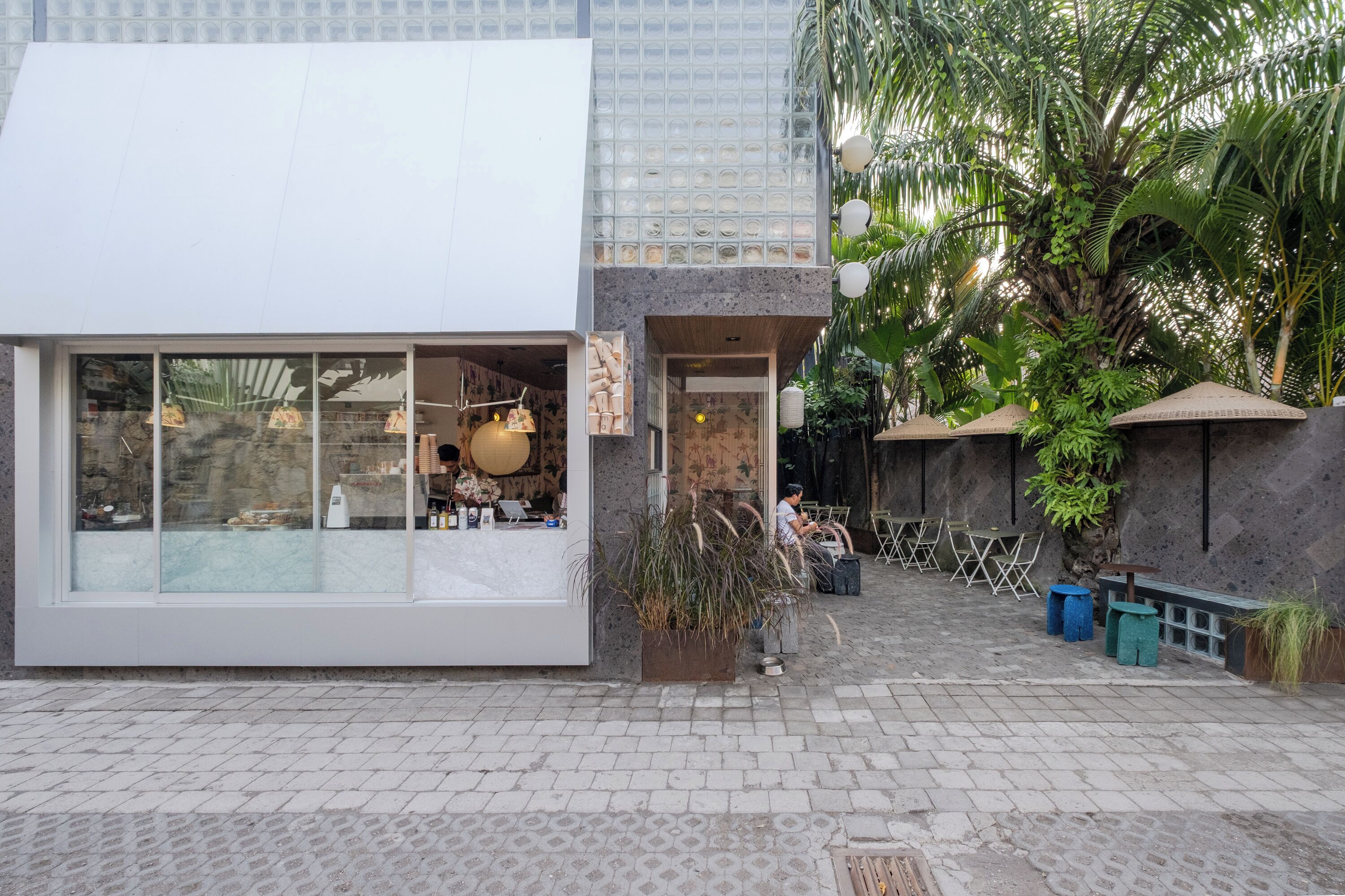A modern building with large glass windows, a stone facade, and outdoor seating.
