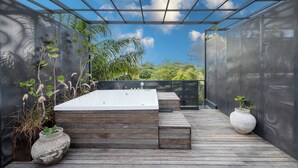 A wooden deck with a hot tub, a white vase, and a pergola with a mesh roof. - The Lima Ocean Suites Pererenan (Canggu)