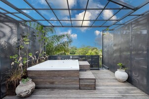 Una terraza de madera con un jacuzzi, un florero blanco y una pérgola con techo de malla.