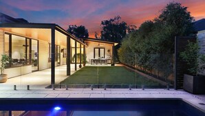 Een modern huis met een zwembad, glazen wanden en een verzorgd gazon.
