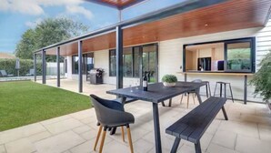 Een terras buiten met een tafel, stoelen, een bank en een barbecuehoek.
