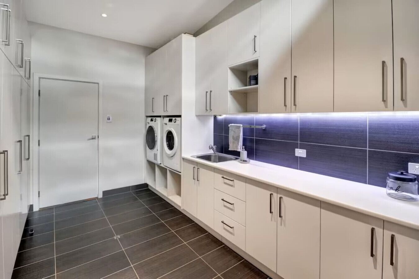 A modern kitchen with a built-in washer and dryer, a sink, and a tiled backsplash.
