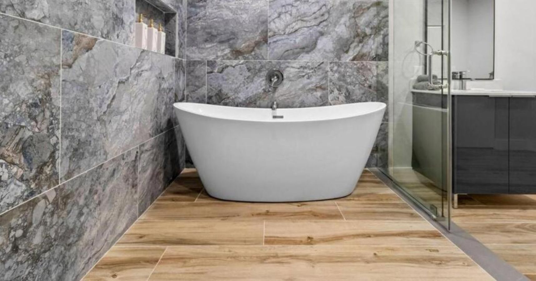 A modern bathroom with a freestanding bathtub, marble walls, and a wooden floor.