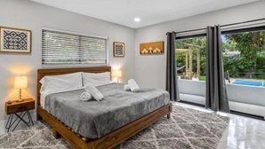 Une chambre à coucher avec un lit, des lampes de chevet, une fenêtre avec des stores et une vue sur la verdure à l’extérieur.