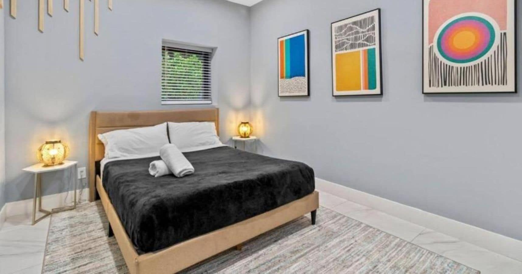 A modern bedroom with a bed, bedside lamps, and abstract wall art.
