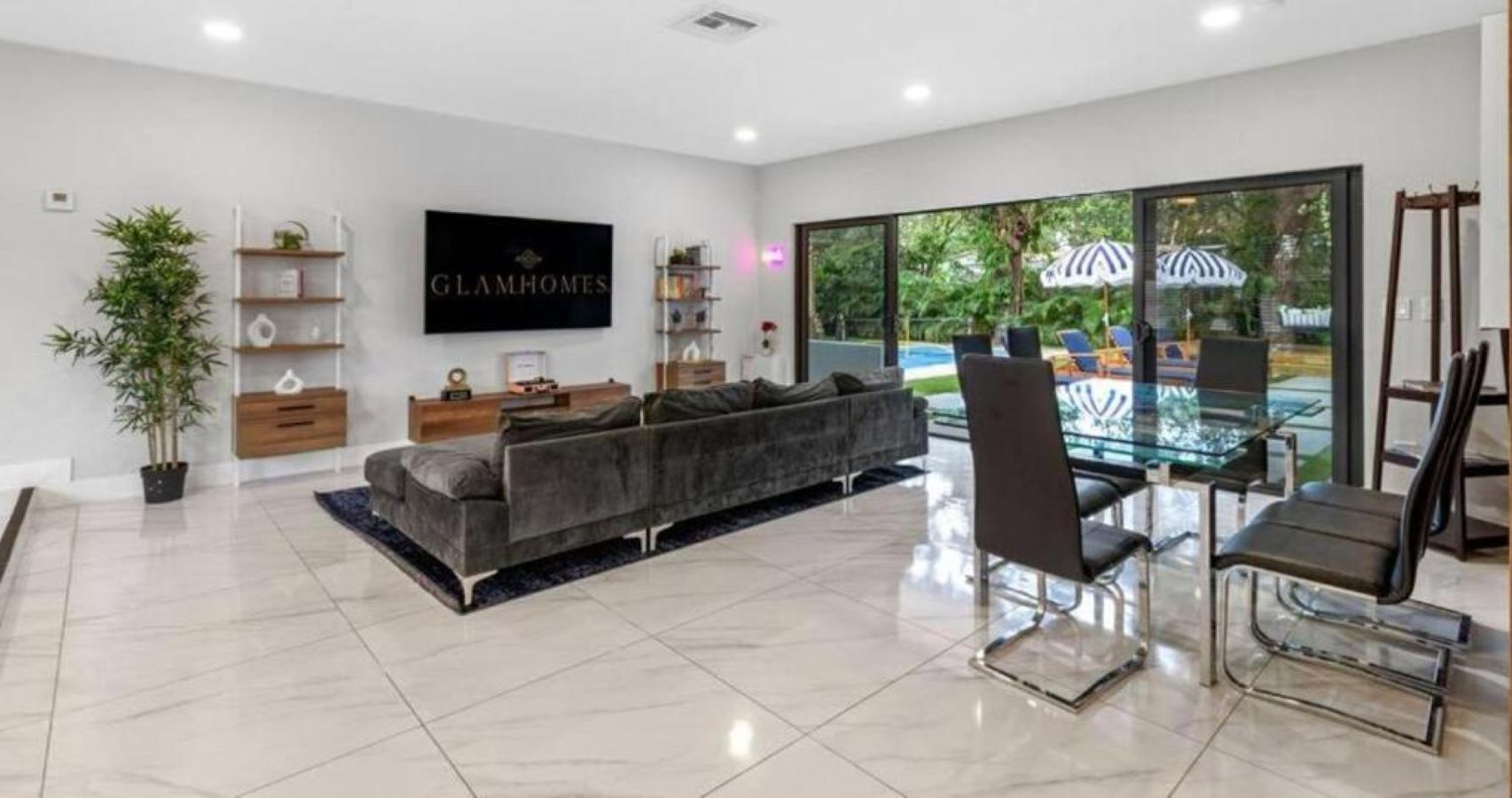 A modern living room with a grey sofa, a glass dining table, and a TV mounted on the wall.
