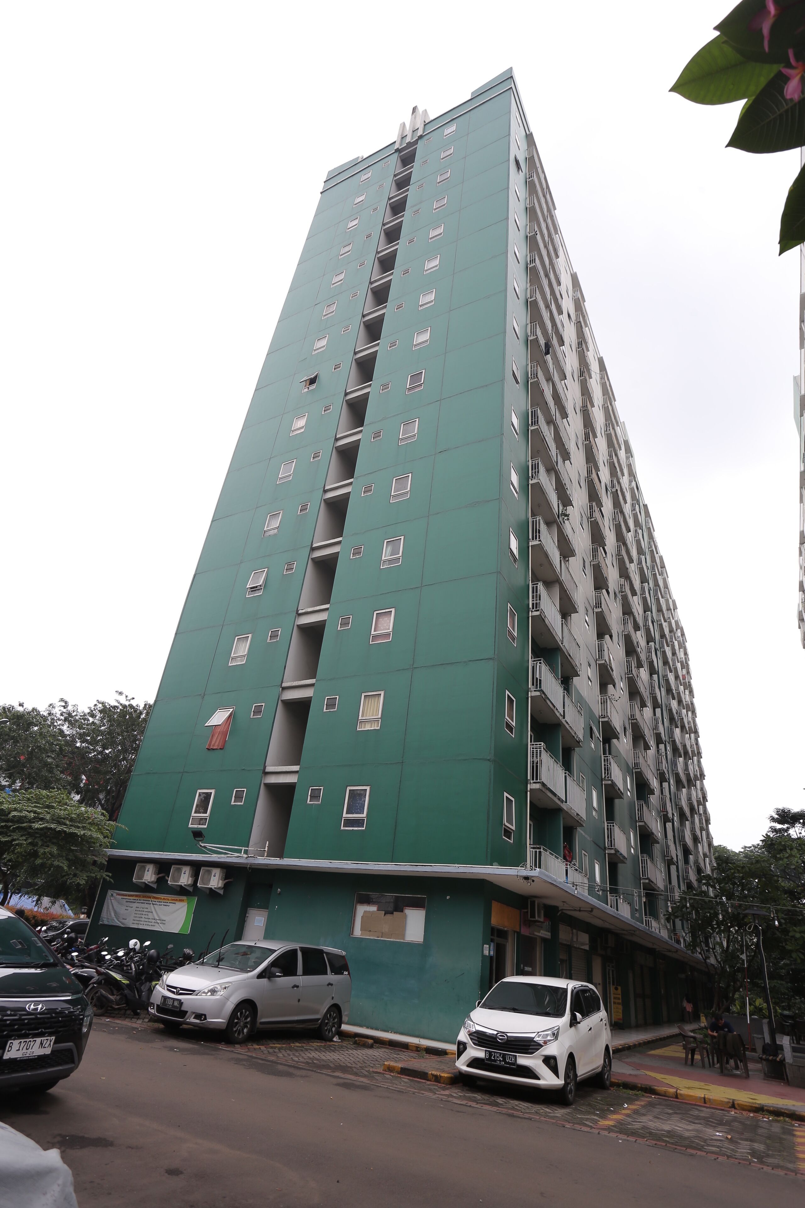 Un grand immeuble à plusieurs étages, doté de balcons, avec des voitures garées devant et une rue qui passe en face.