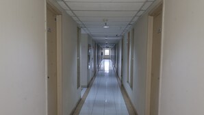 A long, narrow hallway with doors on both sides, a tiled floor, and a ceiling with recessed lighting.