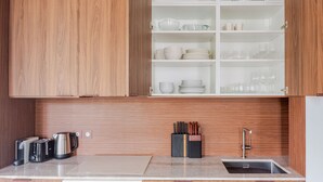 Une cuisine avec des meubles de rangement en bois, un plan de travail sur lequel se trouvent une bouilloire, un grille-pain et un bloc à couteaux, ainsi qu’un évier.