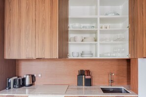 A kitchen with wooden cabinets, a countertop with a kettle, toaster, and knife block, and a sink. - Blueground | Le Marais, washer, nr Pompidou (Paris)