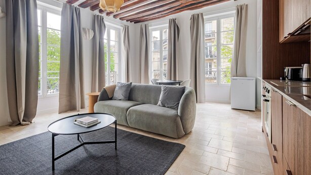 Un salon moderne comprenant un canapé, une table basse et un coin cuisine avec un réfrigérateur et une cuisinière.