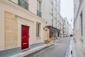 A narrow street with buildings on both sides, a red door, and a bike lane. - Blueground | Le Marais, washer, nr Pompidou (Paris)
