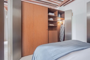 A bedroom with a bed, a wooden wardrobe, and a shelf with folded clothes. - Blueground | Le Marais, washer, nr Pompidou (Paris)
