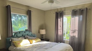 Un dormitorio con cama, mesita de noche, lámpara y ventana con cortinas.