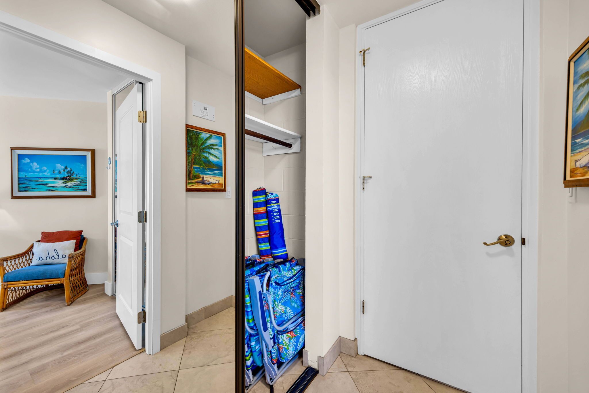 A hallway with a door leading to a room, a wicker chair with a cushion, and a painting on the wall.