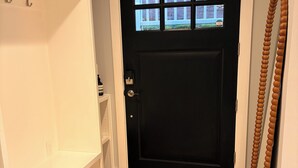 En sort dør med et vindue, en hvid væg, en trædørramme, en dørmåtte og en dekorativ perletråd.