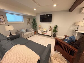 Ein Wohnzimmer mit Sofa, Fernseher, Lampe und einer Pflanze.