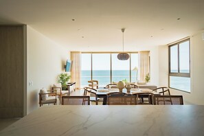 A modern dining area with a large marble table, wicker chairs, and a view of the ocean. - Welcome to Sun & Salt, an oceanfront condominium in El Zonte's Surf City featuring two bedrooms, two and a half bathrooms, a resort-style pool, and space for up to four guests. (El Zonte)