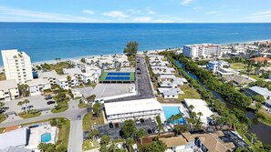 Vue aérienne d’un complexe hôtelier situé sur la côte, avec un court de tennis, un parking et une rivière.