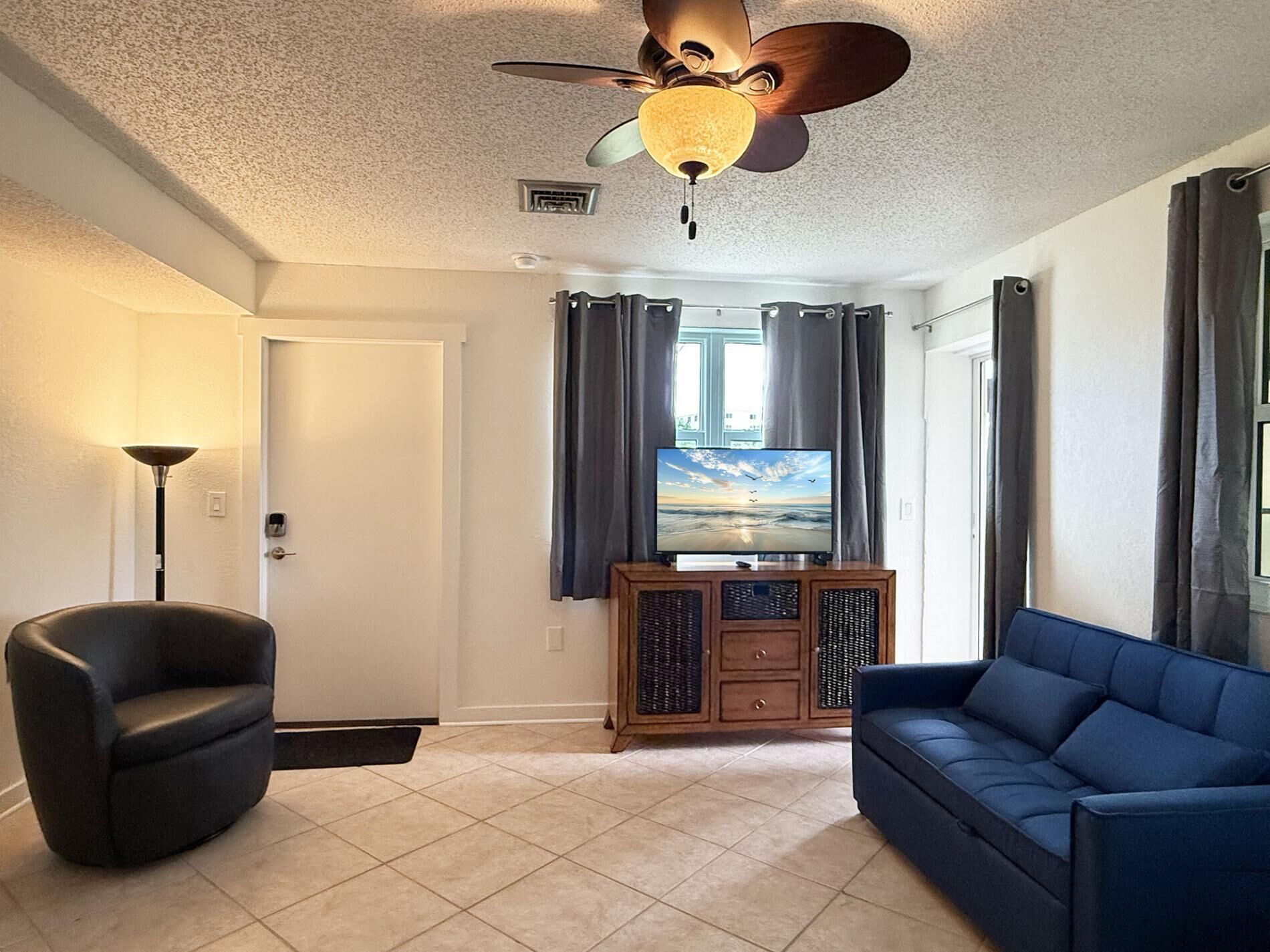 A living room with a ceiling fan, a television on a wooden cabinet, a blue sofa, and a floor lamp.