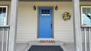 A blue door with a doormat, a welcome mat, and a floral wreath on the porch.