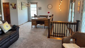 A living room with a black leather sofa, a dining table with a clock, and a staircase.
