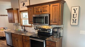 A kitchen with wooden cabinets, a stainless steel microwave, a stove, and a coffee maker.