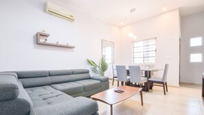 A modern living room with a grey sectional sofa, a wooden coffee table, and a dining area with grey chairs and a glass table.
