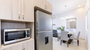 A modern kitchen with a built-in microwave and refrigerator, a dining area with a table and chairs, and a sofa in the background.