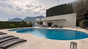 Une piscine avec des chaises longues, un espace salon couvert et des montagnes en arrière-plan.