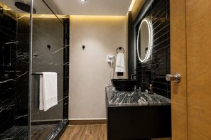 A modern bathroom with a glass-enclosed shower, a vanity with a black sink, and a mirror with LED lights. - Suite Rubí Red Room | Prime Location in Centrito Valle (San Pedro Garza García)