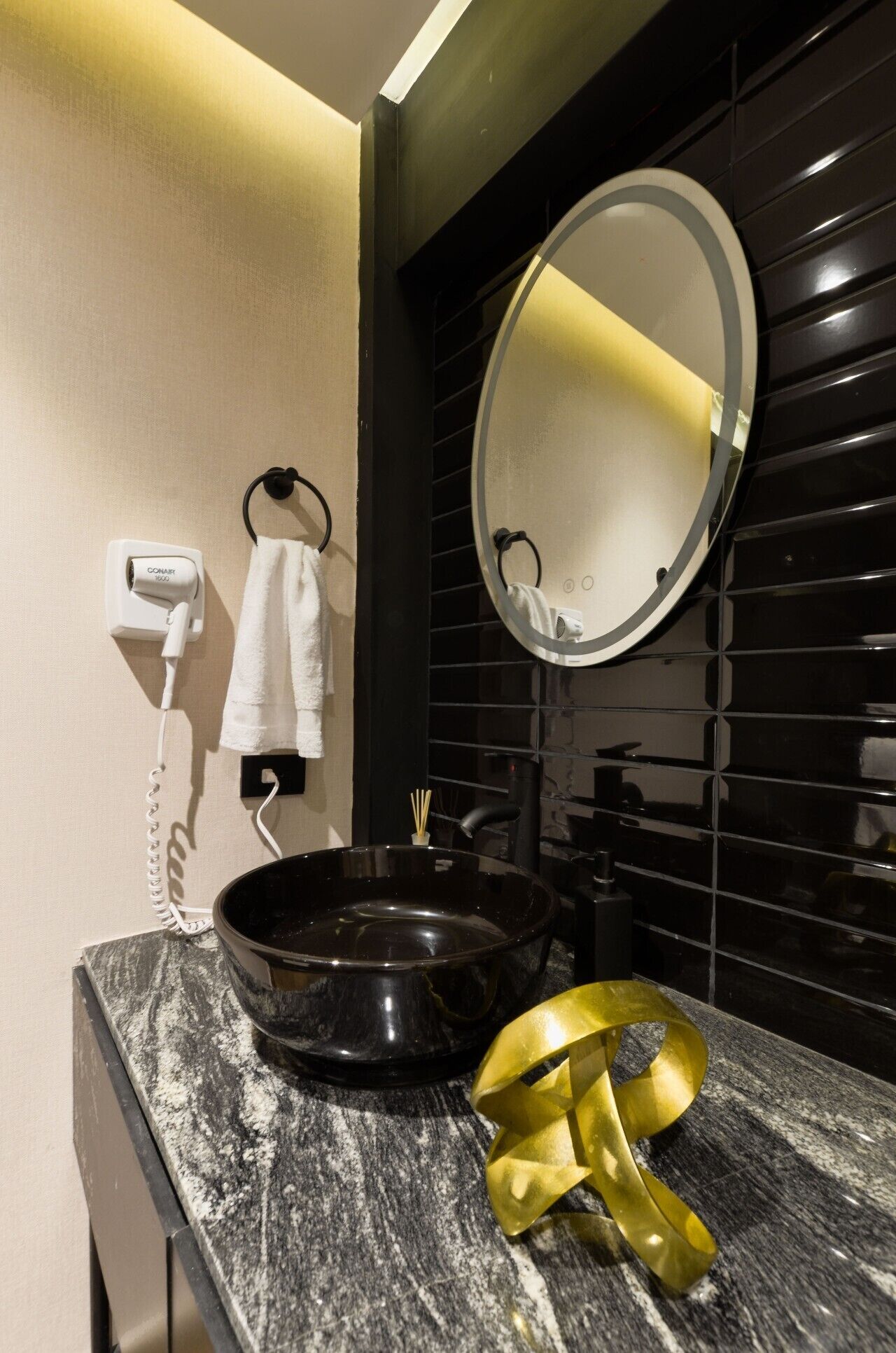 A bathroom with a black sink, a round mirror, a towel rack, and a hairdryer.