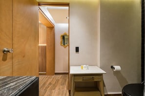 Un baño con puerta de madera, un espejo, un inodoro y un lavabo con artículos de aseo.