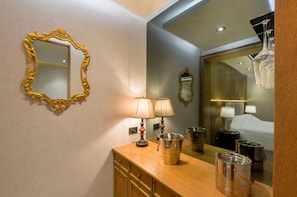 Un baño de hotel con tocador de madera, dos lámparas de pared, un espejo grande y una bañera visible en el reflejo.