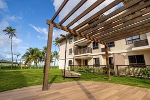 Ein modernes Gebäude mit Balkon, einer Holzpergola und einer Rasenfläche mit Palmen.