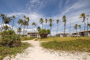 Ein Strandweg führt zu einem Resort mit Palmen und blauem Himmel.