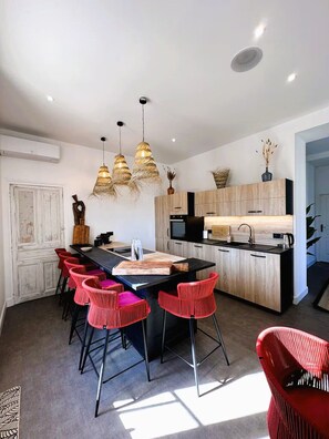 Une cuisine moderne dotée d’un îlot central, de luminaires suspendus et d’un coin repas avec des chaises rouges.