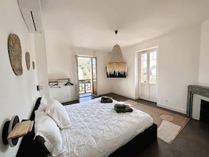 Ein Schlafzimmer mit Bett, einer Pendelleuchte, einer Tür und Blick ins Freie.