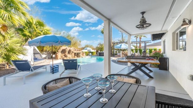 A poolside area with lounge chairs, a table with glasses, a waterfall feature, and a clear sky. - Tropical Villa by Glam Homes (Scottsdale)