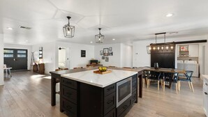 A spacious kitchen with a large island, wooden flooring, and pendant lighting. - Tropical Villa by Glam Homes (Scottsdale)