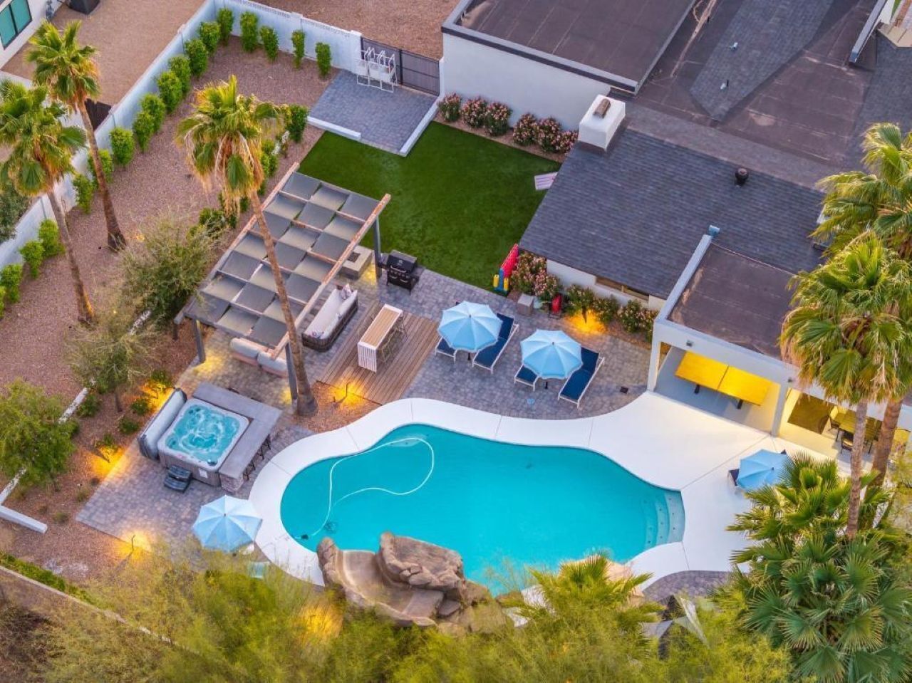 A swimming pool with lounge chairs and umbrellas, surrounded by palm trees and a deck area.