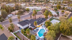 An aerial view of a residential area with a large house featuring a swimming pool, multiple driveways, and surrounding palm trees. - Tropical Villa by Glam Homes (Scottsdale)