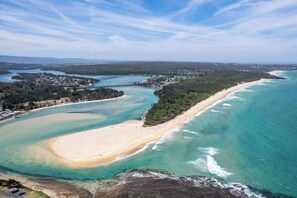 Luftaufnahme einer Küstenlandschaft mit Strand, klarem Wasser und bewaldetem Gebiet.