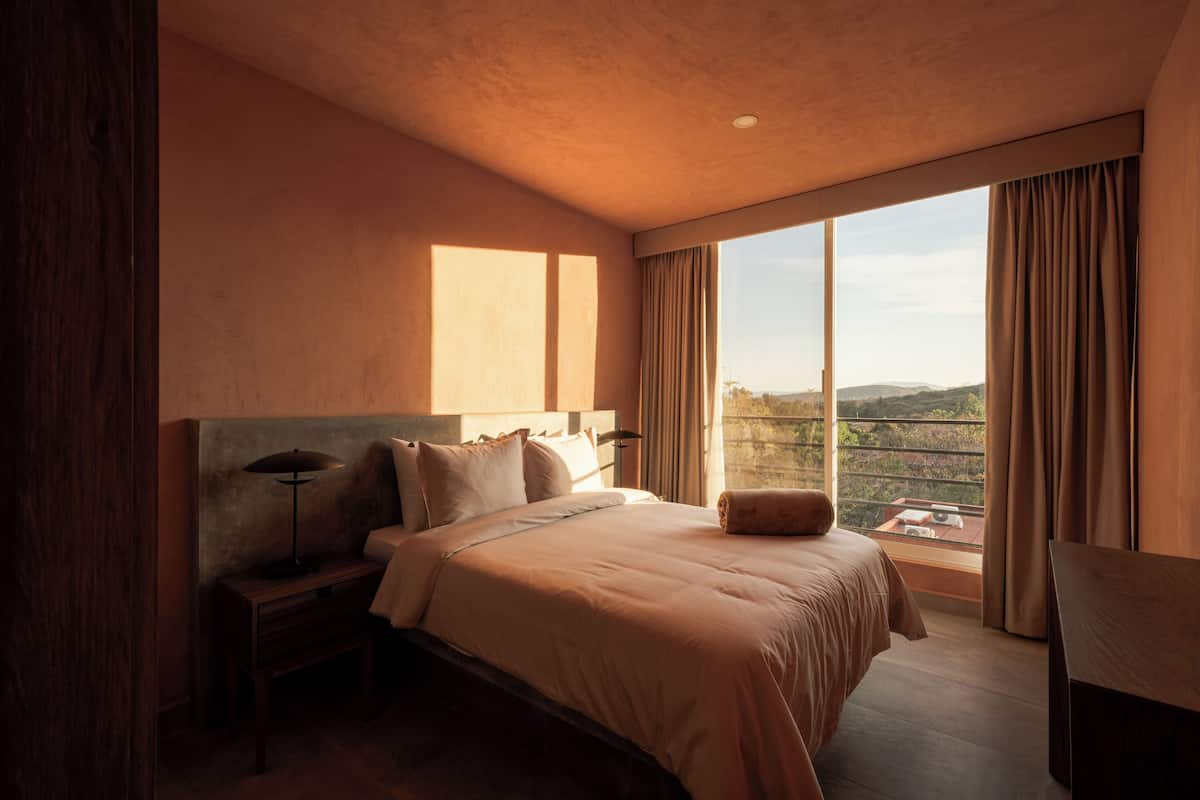 Un dormitorio con una cama grande, una mesita de noche, una lámpara y vistas al exterior.