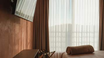 A hotel room with a bed, a desk, a chair, a television mounted on the wall, and a window with curtains.