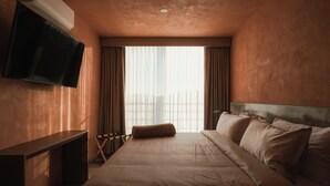 Ein Hotelzimmer mit Bett, einem an der Wand befestigten Flachbildfernseher, einem Schreibtisch und einem fenster mit Vorhängen.