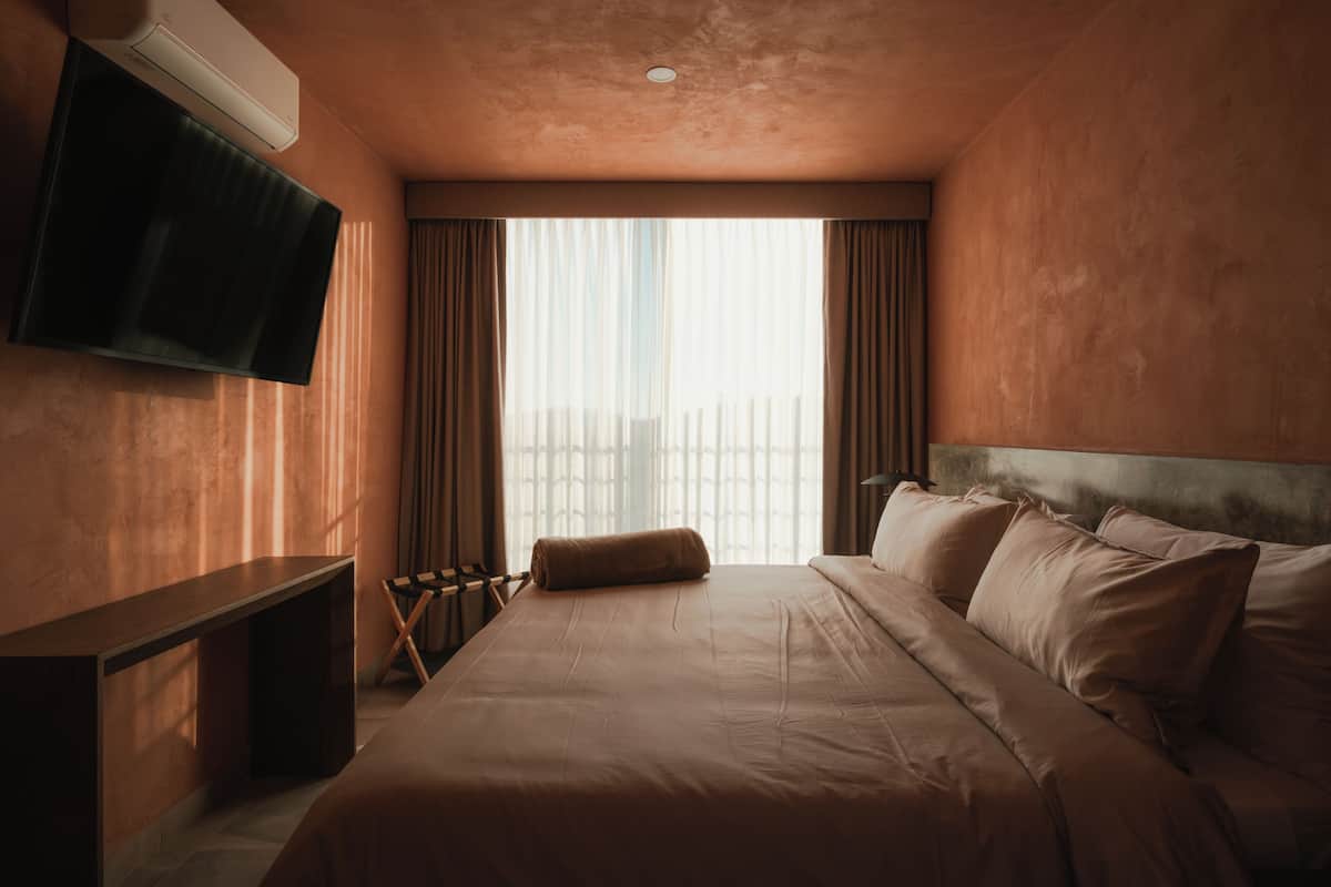 Habitación de hotel con cama, televisor de pantalla plana en la pared, escritorio y ventana con cortinas.